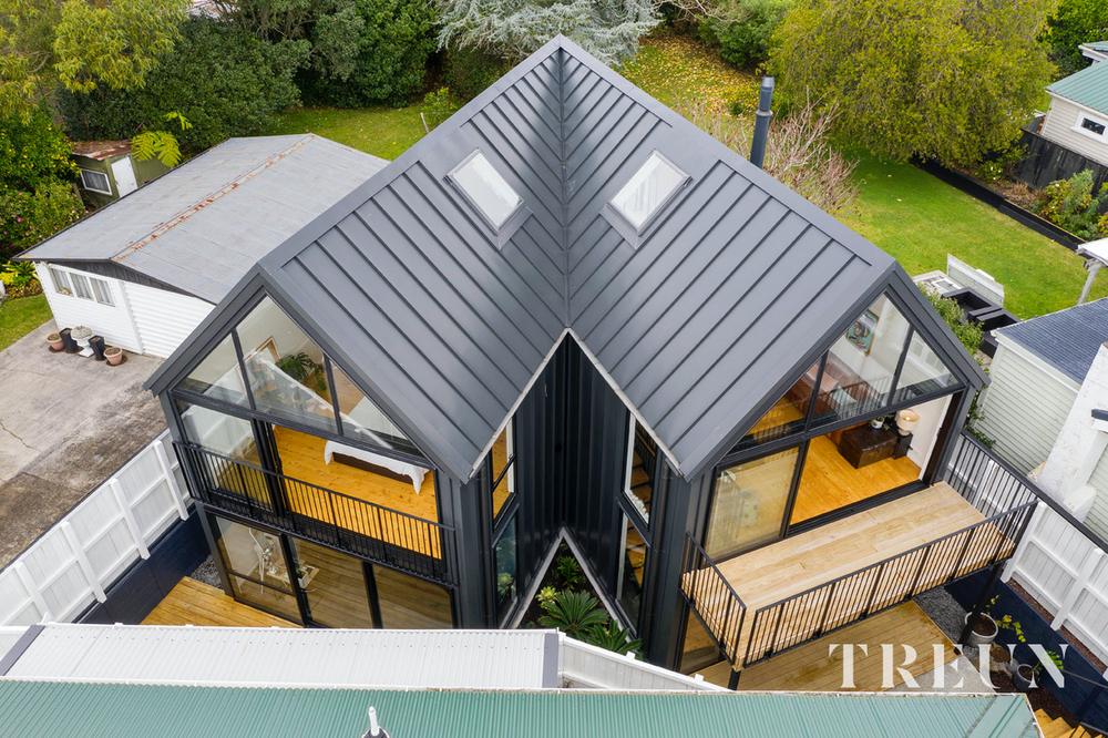 Drone view of an architectural twin-gable home with a dark standing seam longrun roof, skylights and glass gable ends