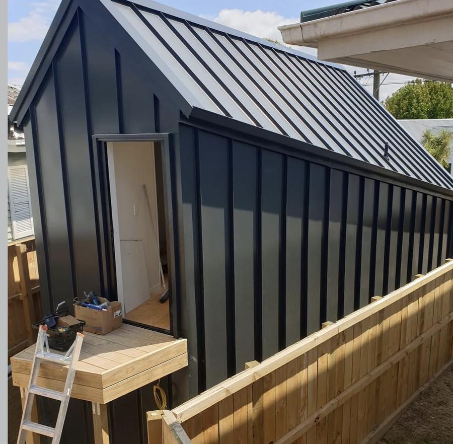 A small sleepout clad and roofed in dark longrun steel with a new timber deck